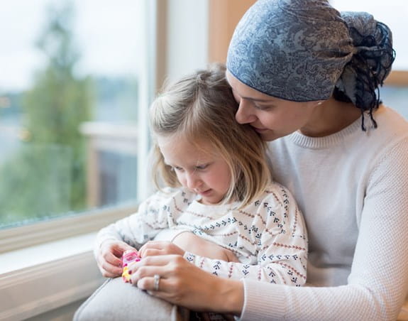 Woman with head scarf sitting by the window with her blond daughter on her lap