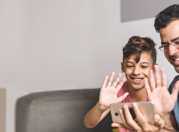 Un père et son enfant, sourient à la caméra d’un téléphone intelligent